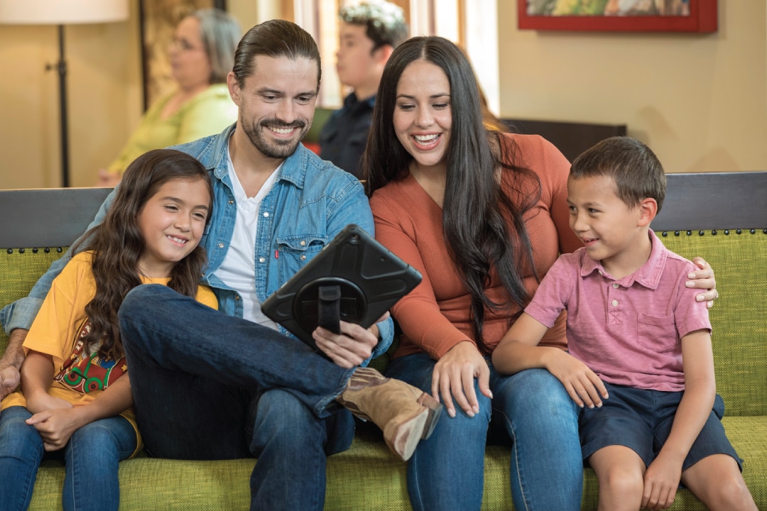 Family sitting together in dental depot waiting room, smiling and filling out paperwork on tablet