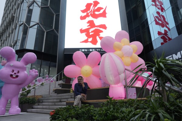 A man makes a call on his phone near the words for Beijing outside a mall in Beijing, Friday, May 24, 2024. The International Monetary Fund has upgraded its forecast for China's economy, while warning that consumer-friendly reforms are needed to sustain strong, high-quality growth. (AP Photo/Ng Han Guan)