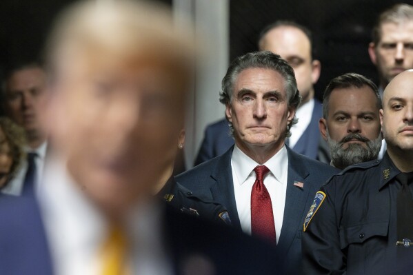 FILE - Republican North Dakota Governor Doug Burgum listens as former President Donald Trump, in foreground, talks to reporters at Manhattan criminal court, May 14, 2024, in New York. Burgum is one of Trump’s most visible and vocal backers, sprinting around the country to drum up support while auditioning to be his running mate. Meanwhile, Burgum is wrestling with a $5.5 billion carbon dioxide pipeline project in his home state. The venture has left him straddling an awkward political divide as Trump and President Joe Biden offer voters starkly different visions of America. (Justin Lane/Pool Photo via AP, File)