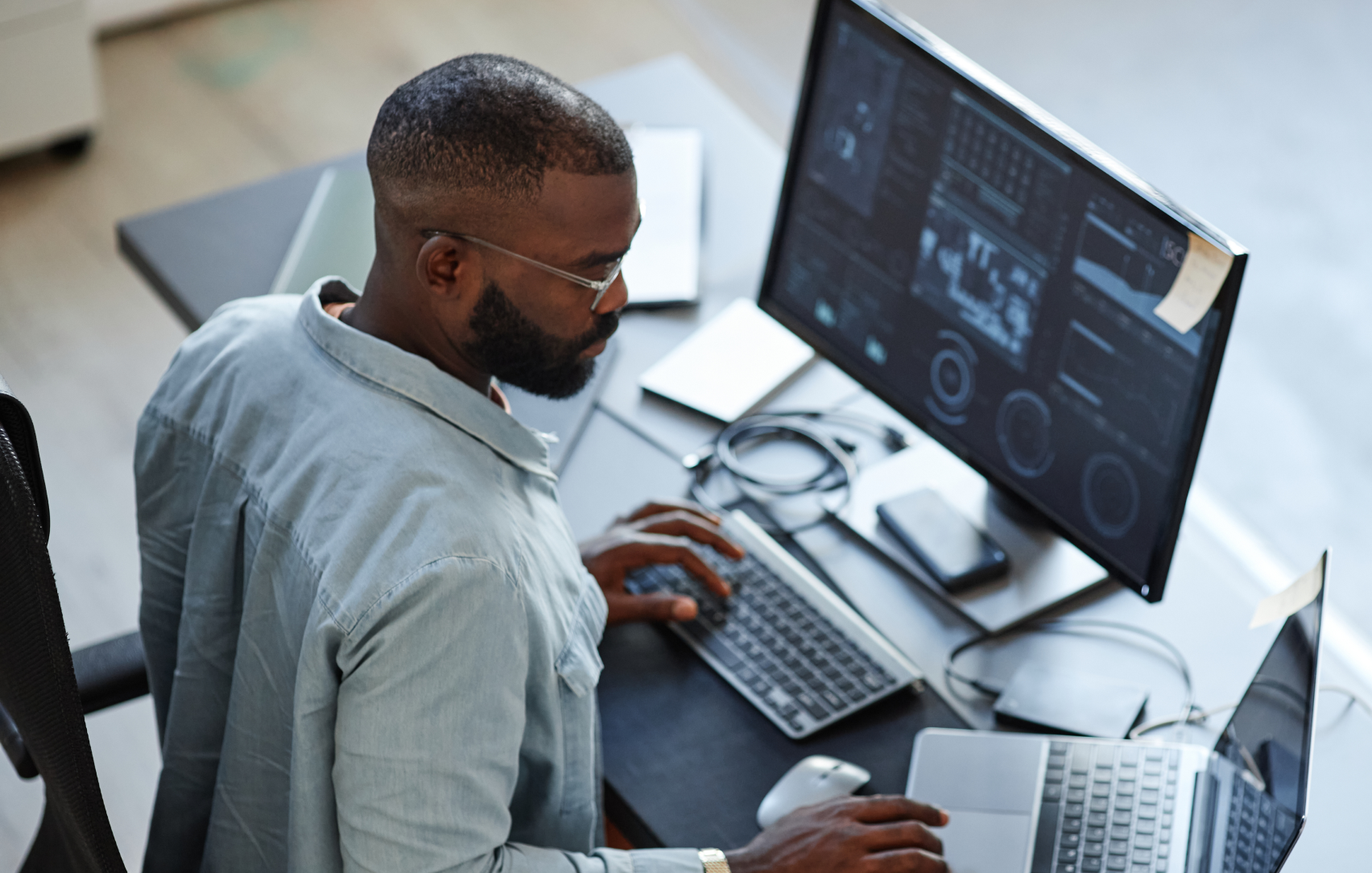 man in an office typing on an external keyboard while browsing on his laptop