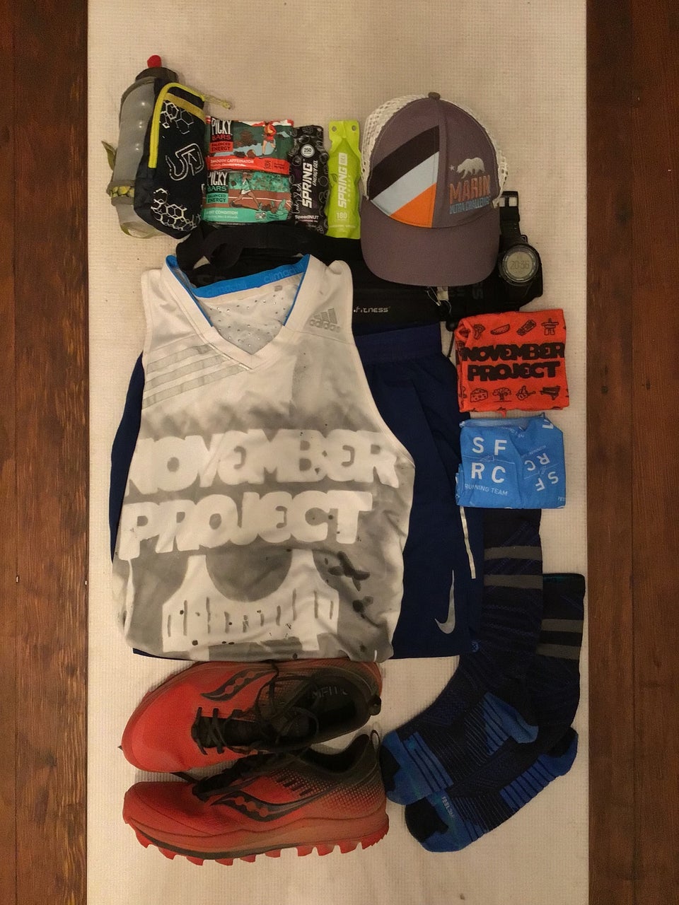 White yoga mat on a hardwood floor with running shoes, clothes, gear, fuel laid out in an orderly fashion.