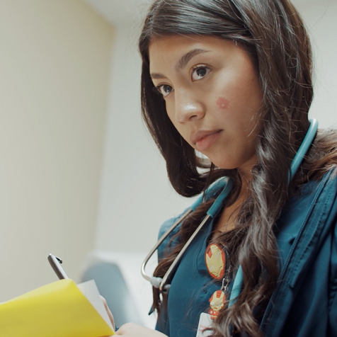 X3 intern wearing scrubs and a stethoscope and taking notes.