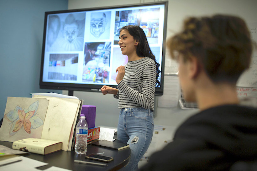 A student standing in front of a screen presenting artwork