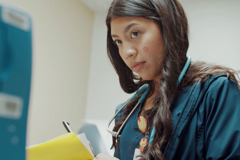 X3 intern wearing scrubs and a stethoscope and taking notes.