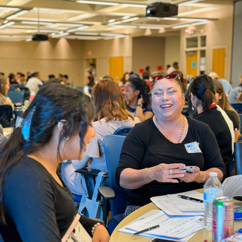 Photo of a crowded conference room with smiling participants seated around tables talking to each other.