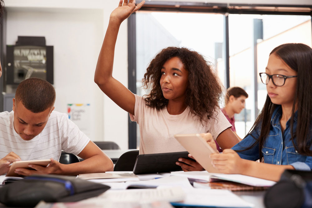 student raising their hand in a classroom.