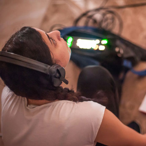 A student wearing headphones looks at something off screen while taking notes.