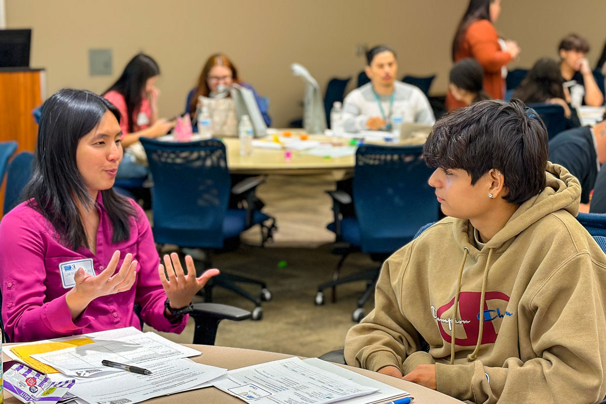 A mentor and student conversing in a crowded conference room.