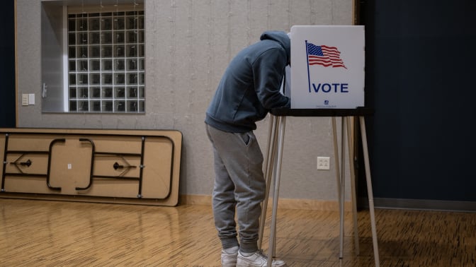 A voter leans over their ballot in a voting booth.