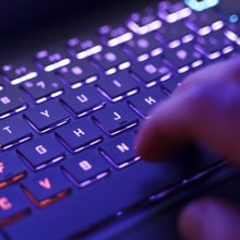 A person working on a neon computer keyboard with colorful backlighting.