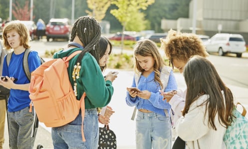 Teens gathered outside of school, all staring at their phones together.