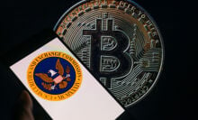 The seal of the U.S. Securities and Exchange Commission is being displayed on a smartphone, with Bitcoin visible on the screen in the background.