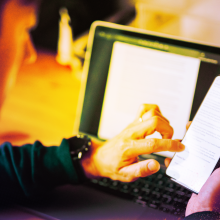 A person sits working at table, using a mobile phone.