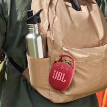 A JBL Clip 4 speaker is clipped onto a backpack