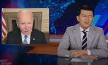 A man in a suit sits behind a talk show desk looking confused. In the top-left is an image of another man on a video call.