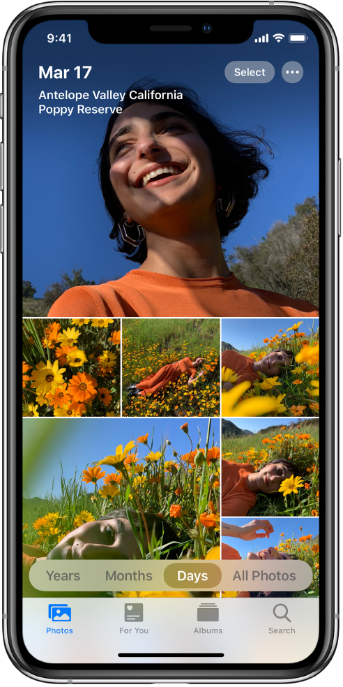 The photo library shown in Days view. A selection of photo thumbnails fills the screen. In the top left of the screen are the date and the location where the photos were taken. In the top right are the Select and More Options buttons; tap Select to share photos and More Options for photo details. Below the thumbnails are options to view the photo library by Years, Months, Days, and All Photos. Along the bottom are the Photos, For You, Albums, and Search tabs.