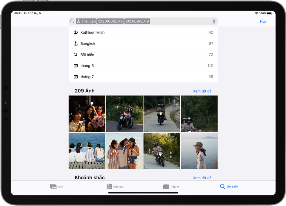 Ảnh được mở ở hướng ngang. Từ trái sang phải ở cuối màn hình là các nút Ảnh, Cho bạn, Album và Tìm kiếm; Tìm kiếm được chọn. Ở đầu màn hình là trường tìm kiếm; một địa điểm và các ngày được nhập trong trường tìm kiếm. Bên dưới trường tìm kiếm, các kết quả tìm kiếm được gợi ý được liệt kê. Một lưới ảnh được tạo ra từ các cụm từ tìm kiếm ở giữa màn hình. Ở trên cùng bên trái của lưới ảnh, tổng số lượng ảnh trong kết quả tìm kiếm được liệt kê. Ở trên cùng bên phải của lưới ảnh là nút Xem tất cả.