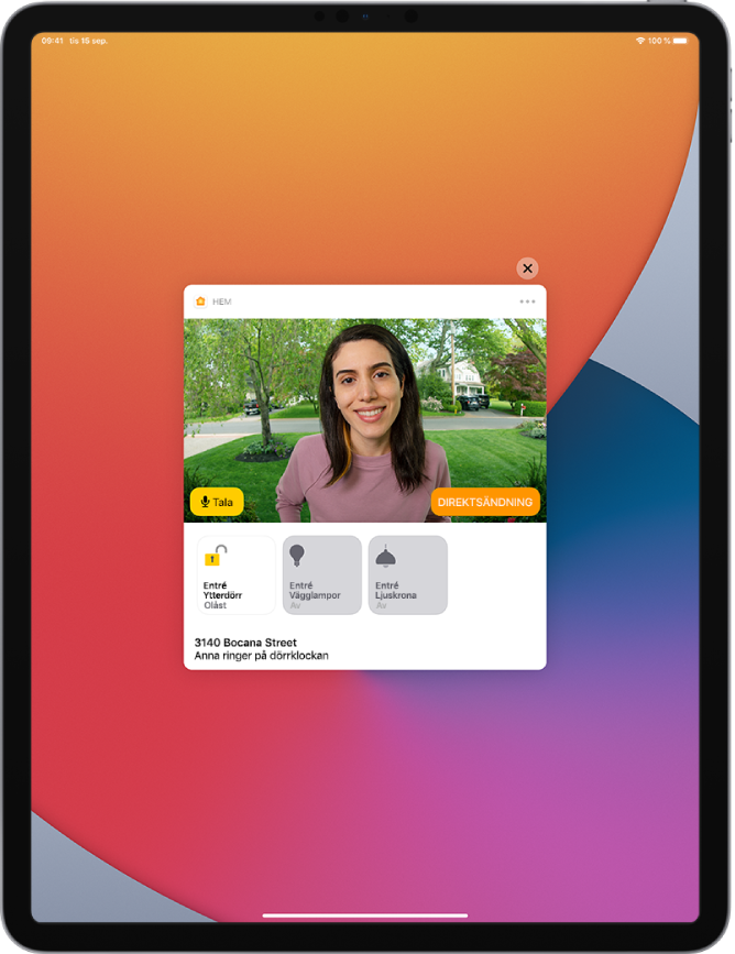 En notis från Hem visas på iPad-skärmen. Den visar bilden på en person vid ytterdörren. Till vänster finns knappen Tala. Under det finns tillbehörsknappar för ytterdörren och entréljus. Hemmets adress visas längst ned tillsammans med orden ”Ashley ringer på dörrklockan”. Högst upp till höger på notisen finns en stängningsknapp.