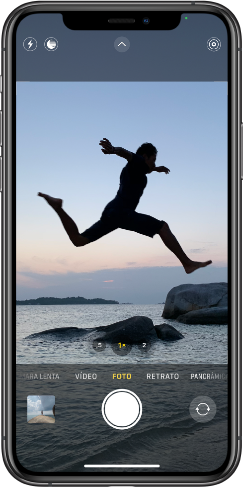 Pantalla Cámara en modo Foto con otros modos a la izquierda y a la derecha debajo del visor. Los botones de Flash, modo Noche, “Controles de cámara” y Live Photo están en la parte superior de la pantalla. Debajo de los modos de cámara están, de izquierda a derecha, el botón “Visor de fotos y vídeos”, el botón “Hacer foto” y el botón selector de la cámara trasera.