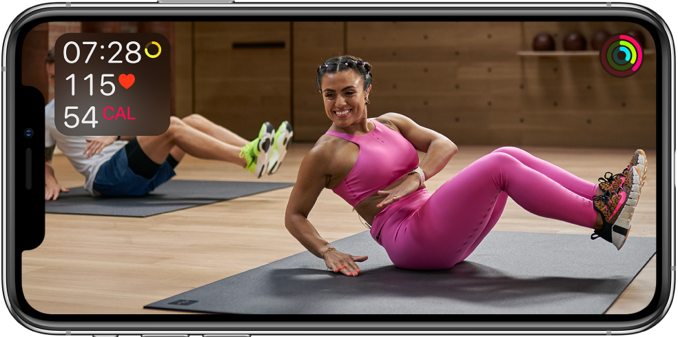 Ecran prezentând un instructor conducând un exercițiu Apple Fitness . Informațiile despre durata exercițiului, ritmul cardiac și caloriile arse apar în partea stângă sus. Inelele de evoluție pentru obiectivele de mișcare, antrenament și stat în picioare apar în dreapta sus.