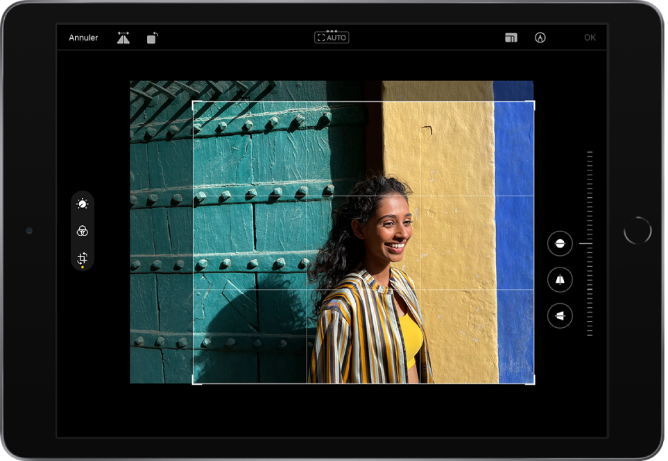 L’iPad en orientation paysage. Au centre de l’écran se trouve une photo en mode édition avec une grille en superposition et un cadre pour recadrer l’image. Sur le côté gauche de l’écran se trouvent les boutons Ajuster, Filtres et Recadrer ; le bouton Recadrer est sélectionné. Sur le côté droit de l’écran se trouvent les options d’amélioration du recadrage et le curseur d’intensité. Dans le coin supérieur gauche se trouvent les boutons Annuler, Retourner et Pivoter. Dans le coin supérieur droit se trouvent les boutons Proportions, Annoter et OK.