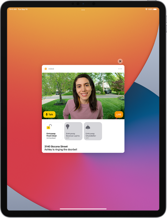 „Home“ pranešimas rodomas „iPad“ ekrane. Jame rodoma prie durų esančio asmens nuotrauka ir kairėje pateikiamas mygtukas „Talk“. Žemiau yra įėjimo durų ir tako apšvietimo priedų mygtukai. Apačioje pateikiami namų adresas ir žodžiai „Ashley skambina durų skambučiu“. Pranešimo viršuje, dešinėje yra uždarymo mygtukas.