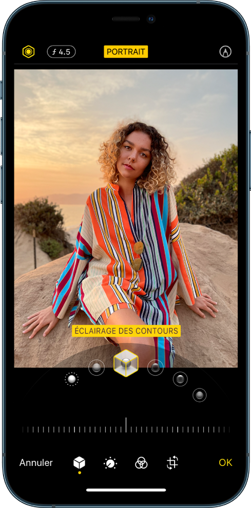 L’écran Modifier d’une photo prise en mode Portrait. En haut à gauche de l’écran se trouvent les boutons « Intensité de l’éclairage » et « Réglage de la profondeur ». En haut, au centre de l’écran, le bouton Portrait est activé. En haut à droite se trouve le bouton Annoter. La photo est au centre de l’écran ; sous celle-ci se trouve un curseur permettant de choisir l’effet d’éclairage de portrait. En dessous se trouve un curseur permettant d’ajuster la valeur de l’effet. En bas de l’écran, de gauche à droite, se trouvent les boutons Annuler, Portrait, Ajuster, Filtres, Recadrer et OK.