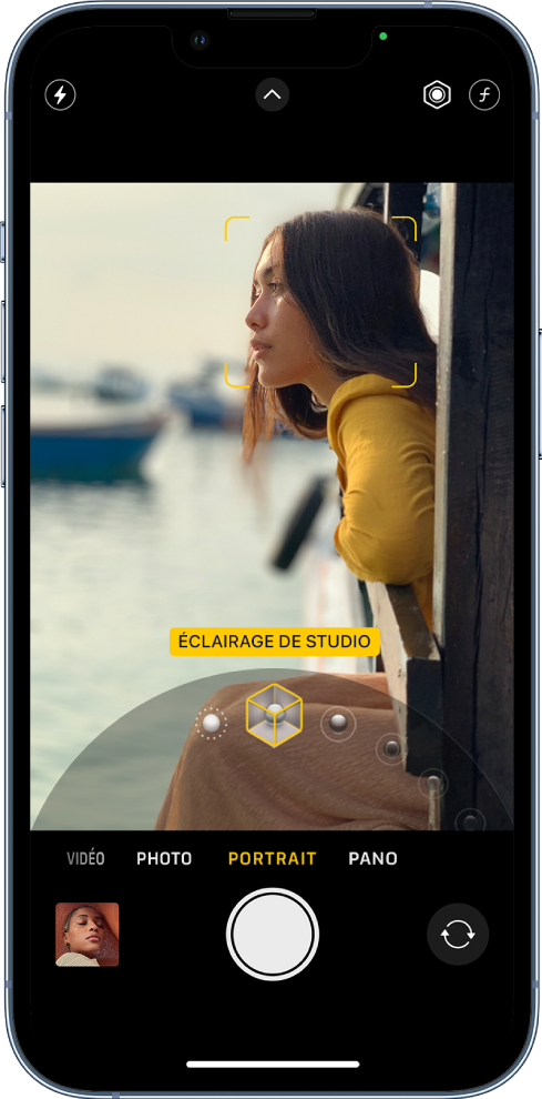 L’écran « Appareil photo » en mode Portrait ; dans le viseur, le sujet est net tandis que l’arrière-plan est flou. Le cadran pour sélectionner les effets d’éclairage Portrait est ouvert en bas de l’image et « Éclairage de studio » est sélectionné. En haut à gauche de l’écran se trouve le bouton Flash, en haut au centre se trouve le bouton « Commandes de l’appareil photo », et en haut à droite de l’écran se trouvent les boutons permettant de régler l’intensité lumineuse du portrait et le contrôle de la profondeur. En bas de l’écran, de gauche à droite, se trouvent le bouton « Visualiseur de photos et vidéos », le bouton « Prendre une photo » et le bouton « Sélecteur de caméra - face arrière ».