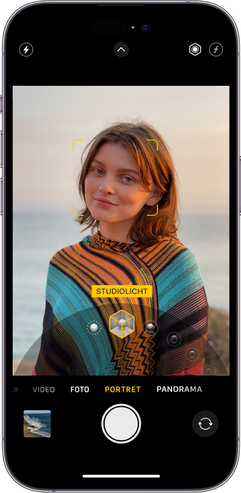 Het Camera-scherm in de portretmodus. Het onderwerp in de zoeker is scherp en de achtergrond is wazig. De draaiknop om portretbelichtingseffecten te kiezen is open onder in het beeld en 'Studiolicht' is geselecteerd. Linksboven in het scherm bevindt zich de flitserknop, in het midden bovenaan bevindt zich de knop 'Cameraregelaars' en rechtsboven in het scherm bevinden zich de knoppen om de intensiteit van de portretbelichting en de scherptediepte aan te passen. Onder in het scherm staan van links naar rechts de knop 'Foto- en videoweergave', de knop 'Maak foto' en de knop voor het kiezen van de camera aan de achterkant.