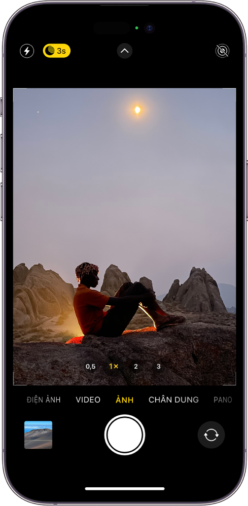 Màn hình Camera ở chế độ Ảnh. Bên trong kính ngắm là một cảnh ban đêm. Các nút cho flash và chế độ Ban đêm ở góc trên cùng bên trái của màn hình và chế độ Ban đêm được bật. Nút Điều khiển camera ở trên cùng ở giữa và nút Live photos ở góc trên cùng bên phải. Ở cuối màn hình, từ trái sang phải, là nút Trình xem ảnh và video, nút Chụp ảnh và nút Chọn camera mặt sau.