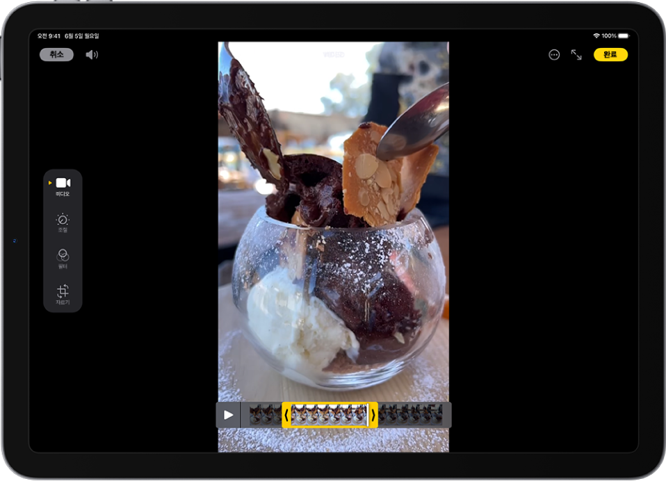 중앙에 비디오가 재생 중인 사진 앱의 편집 화면. 비디오의 프레임 뷰어는 비디오 하단을 가로지르고 다듬은 비디오에 포함하기 위해 선택한 프레임 주변에 노란색 테두리가 표시됨. 화면 왼쪽에 비디오, 조절, 필터 및 자르기 버튼이 나열되고 비디오 버튼이 선택됨.
