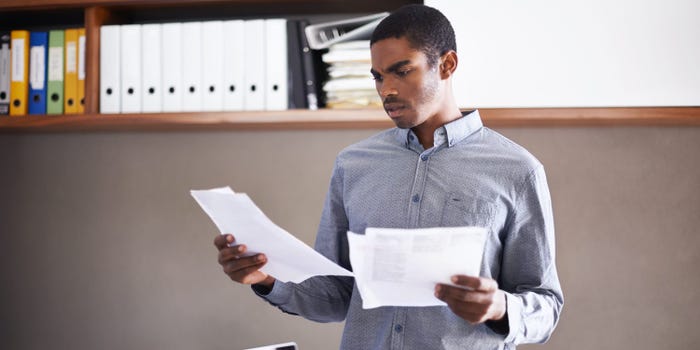 A photo of a man viewing papers about bonds and CDs while standing in an office.