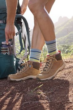 a person wearing hiking shoes and socks standing next to a backpack