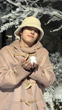 This may contain: a woman wearing a coat and hat holding an apple in front of snow covered trees