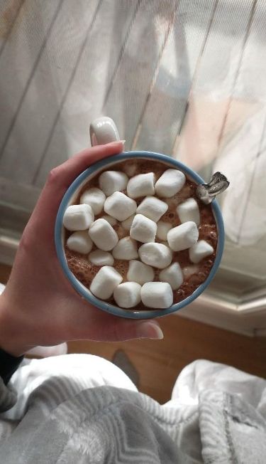 This may contain: a person holding a bowl of hot chocolate with marshmallows