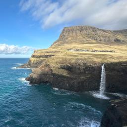  Der Wasserfall Mulafossur stürzt in der Ortschaft Gasadalur in den Nordatlantik. Im Hintergrund ist die Insel Mykines zu sehen.