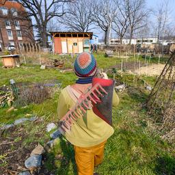 Ein Mitglied des Gemeinschaftsgartens Wurzelwerk Pieschen läuft mit Gartengeräten durch die Anlage.