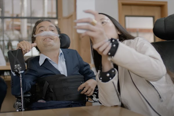 Googler Aubrie Lee (she/her) sits in her wheelchair and takes a selfie with a man in a wheelchair