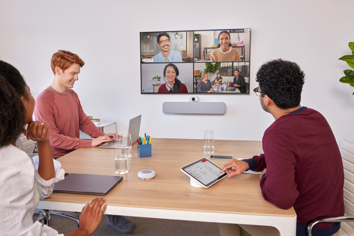 A meeting room with three people and four shown on-screen in video conference