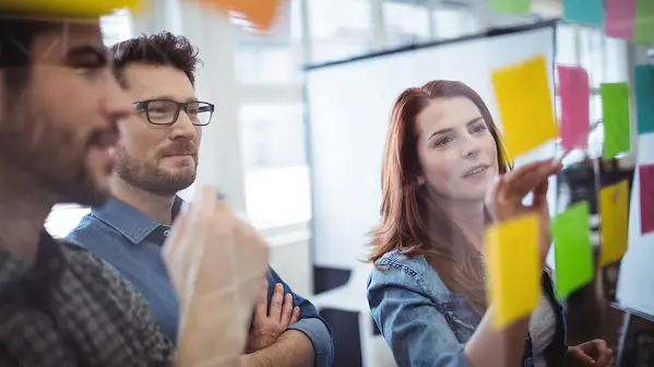 A group of coworkers in a meeting room putting sticky notes on the glass wall