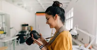 Egy nő mosolyog, miközben DSLR fényképezőgépet használ.