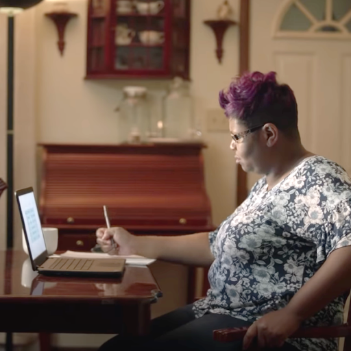 A Black woman with glasses works on her laptop at home