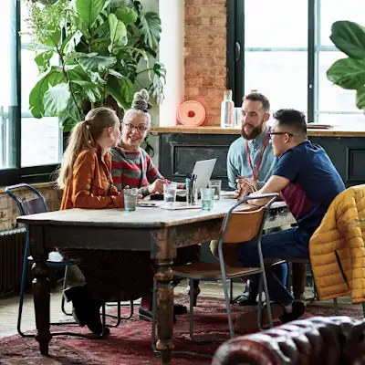 Quatre collègues sont assis autour d’une table de réunion, entourés de plantes dans un environnement de travail luxuriant.