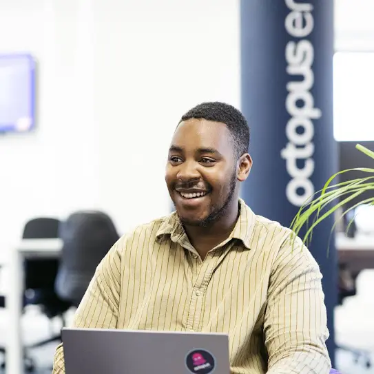 Man sitting in an Octopus Energy office, smiling with a laptop in front of him.