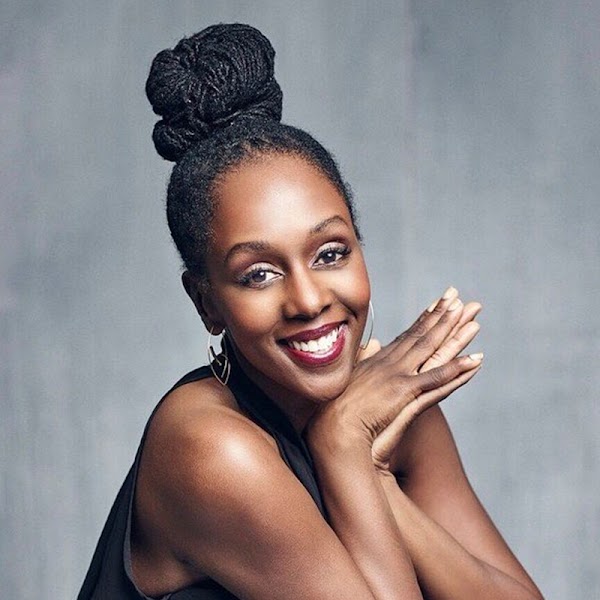 Portrait of artist smiling with their hands clasped wearing individual braids pulled up into a bun.