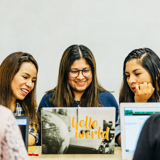 Tres mujeres jóvenes sentadas en el escritorio mirando la computadora portátil