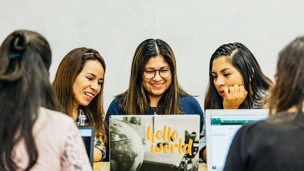 Tres mujeres jóvenes sentadas en el escritorio mirando la computadora portátil