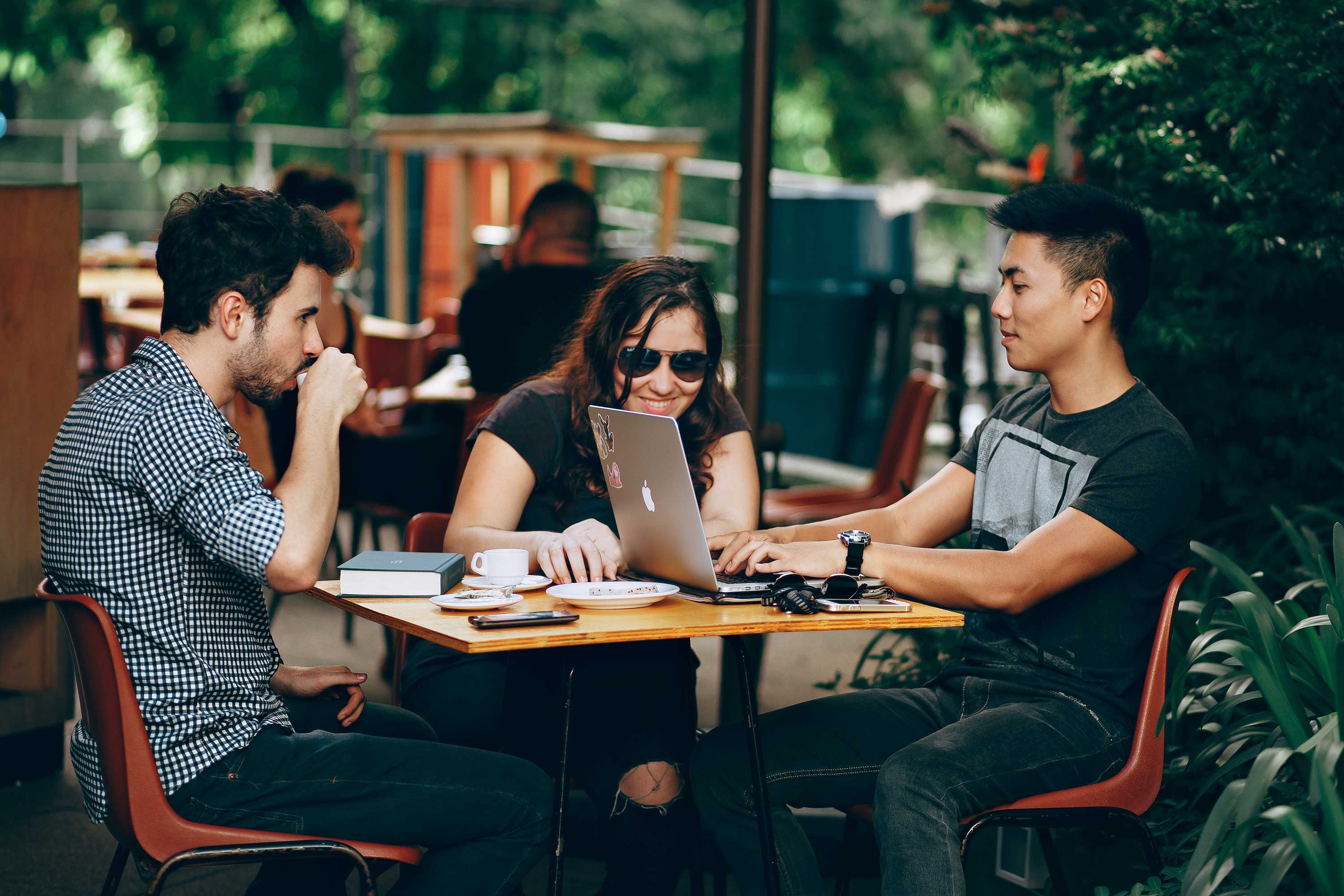 3 young adults sit around table working on laptops