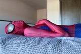 A person in a Spider-Man suit rests on a bed, embodying a casual demeanor in his signature superhero attire.