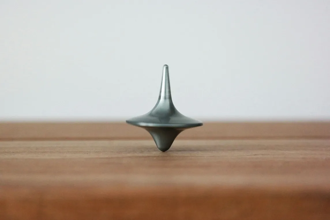 Silver metal top spinning vertical on a wooden table with a white background.